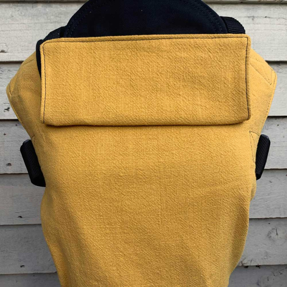 Integra eco-friendly ochre linen baby carrier in front of a wooden fence