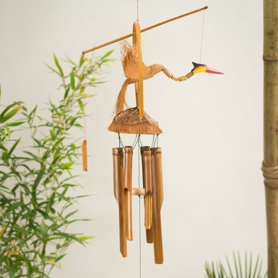 Namaste Bamboo Windchime with Nodding Bird decoration pictured hanging up with plants in the background 