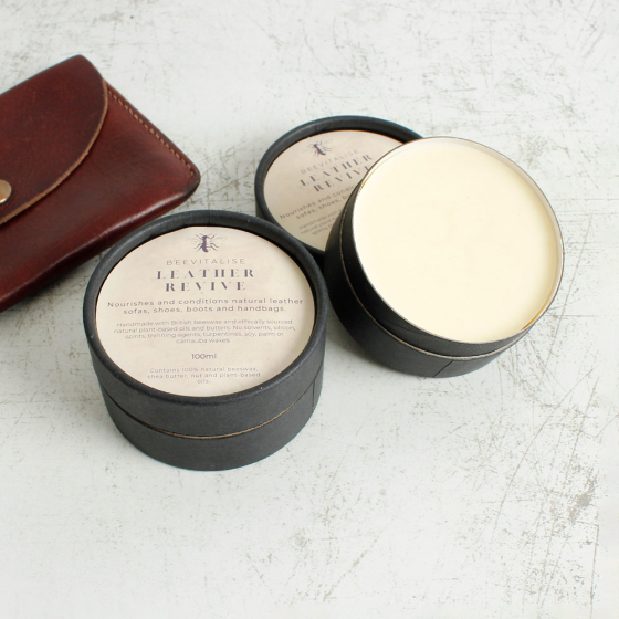 2 tubs of Oakdale Bees beevitalise leather revive balm on a white background next to a brown leather wallet