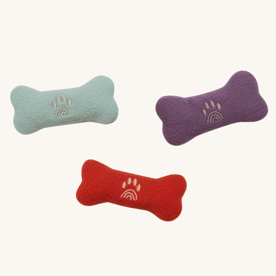 The Olli Ella Dinkum Dogs Bones Pack includes three soft plush dog bone toys to accessorize your Dinkum Dog. One is a pale blue colour, another is purple, and another is red. They all include an embroidered rainbow-shaped paw print.