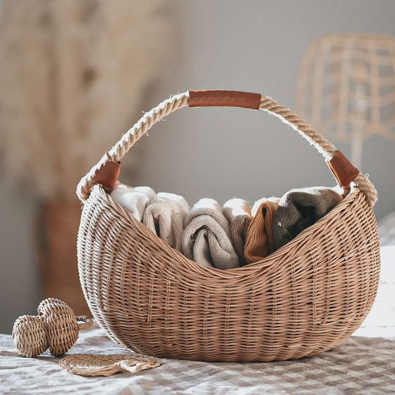 Olli Ella handmade natural rattan half moon basket, filled with coloured fabrics on a checkered tablecloth