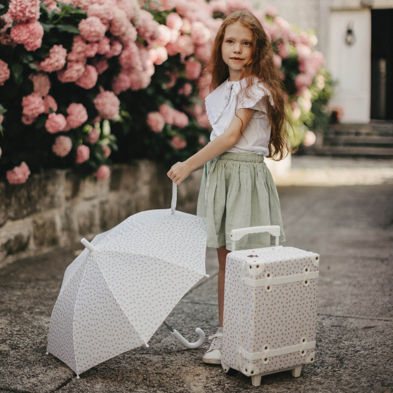 Olli Ella See-Ya Kids Leafed Mushroom Umbrella being held by a child stood next to and Olli Ella Travel Case