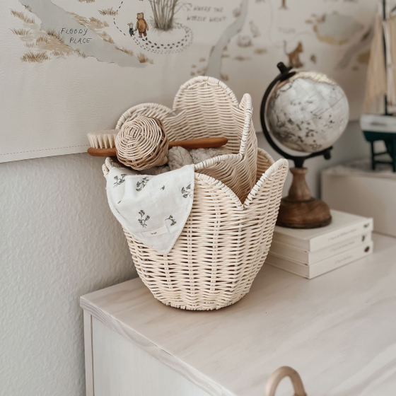 The Olli Ella Rattan Lily Basket Set in Buttercream on a chest of draws in a nursery, nesting together holding baby essentials. Theres a globe in the background and map on the wall.