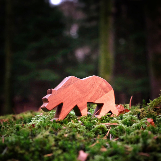 close up of an O-WOW Walnut Bear toy placed on some green moss on a forest floor