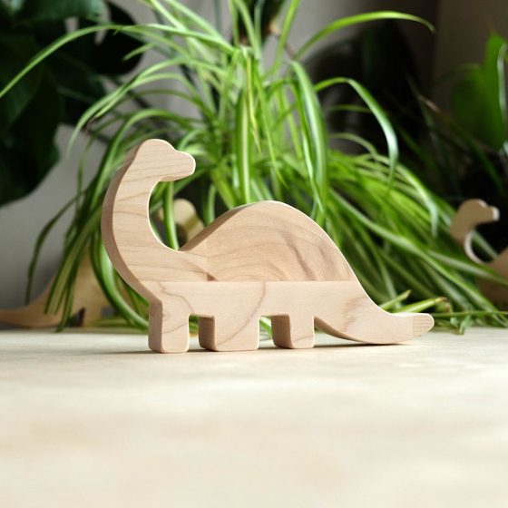O-WOW sustainable wooden diplodocus toy on a wooden worktop in front of a green house plant