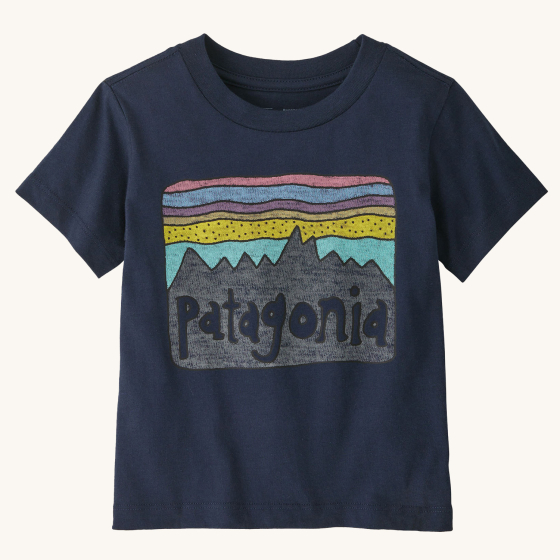 Patagonia Little Kids Fitz Roy Skies T-Shirt - New Navy. A deep, navy blue t-shirt with a fun Patagonia mountain range print in front of a striped pink, blue, purple and yellow sky