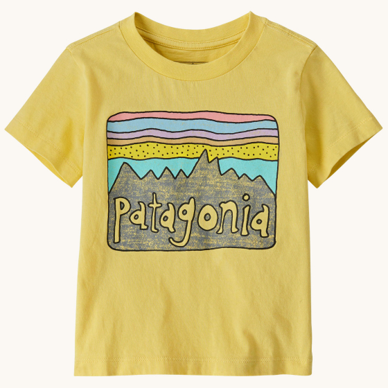 Patagonia Little Kids Fitz Roy Skies Regenerative Organic Cotton T-Shirt - Milled Yellow. A sandy yellow with the classic Fitz Roy Skies colourful mountain scene graphic across the front, on a cream background