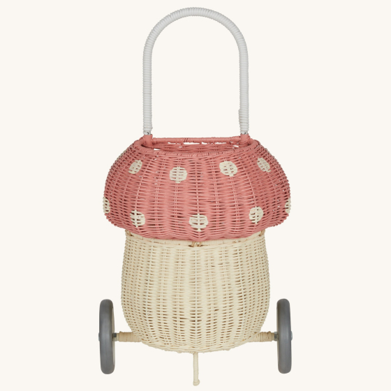 Olli Ella rattan luggy with wheels, in the shape of a mushroom with white spots on a pale pink background.