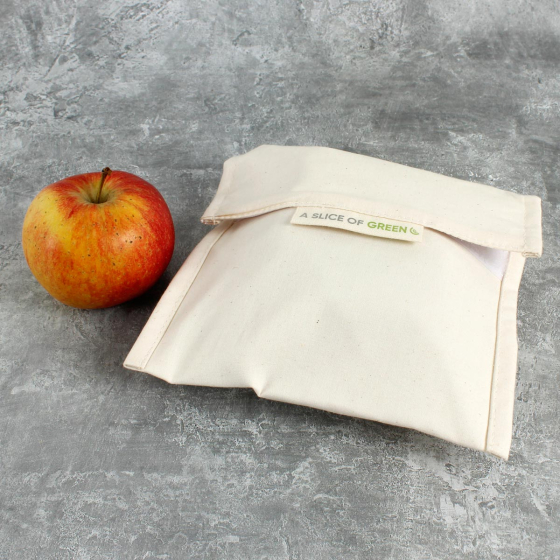 A Slice of Green large organic cotton food baggie on a grey background next to an apple