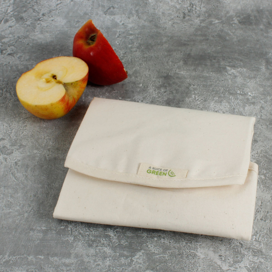 A Slice of Green reusable organic cotton sandwich wrap folded on a grey background next to an apple