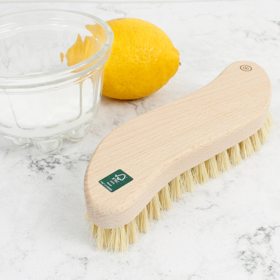 A Slice of Green plastic-free wooden scrubbing brush on a white background next to a lemon and pot of salt