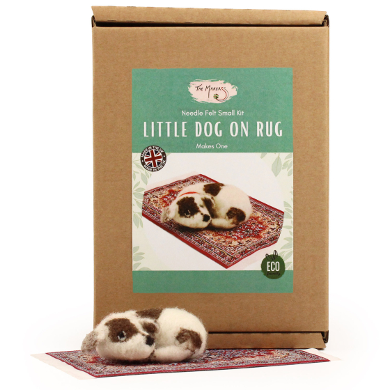 The Makerss Needle Felt Little Dog On Rug. A beautifully crafted white and brown spotted dog on a decorative rug, laying next to its box