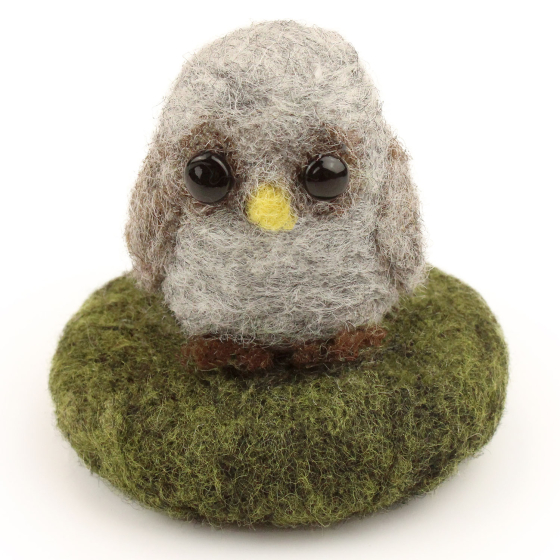A made The Makerss - Amiguwoolli Tiny Owl Mini Needle Felt Figure. The owl is made from grey and brown felting wool, brown feet and a yellow beak, with stick in eyes. The owl is sat on a felted green base