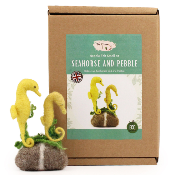 The Makerss Needle Felt Seahorses. Two beautifully crafted yellow Seahorses with green seaweed details, next to each other on a grey and white pebble, next to their box
