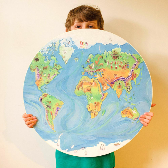Boy stood holding the Waldorf family eco-friendly wooden global map in front of a cream wall