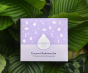 Kokoso Coconut Bathtime Organic Baby Gift Set in its purple and white gift box sitting on a backdrop of large Green leaves