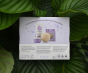 The reverse of the Kokoso Newborn Essentials Organic Baby Gift Set in its purple and white gift box sitting on a backdrop of large Green leaves. The words "Pure and gentle skincare for brand new babies" stand out.