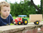 Toddler playing outside with the Bajo wooden tractor and Trailer toy, made from solid hardwood with a red, green and blue painted finish and natural wood trailer. 