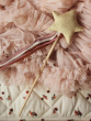 Avery Row Gold Kitted Sparkle wand Toy - Perfect for toddlers who love to play dress up. Wand has a gold knitted star, pink, white and orange ribbons on a wooden stick. On a pink, fabric back ground