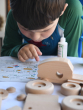 Child reading the Bajo Build A Wooden Toy Tractor - DIY Construction Kit instructions, with wooden tractor pieces and glue on a white table