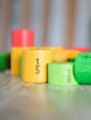 Bajo Fraction Set Maths Resource Learning Toy showing wooden Bajo fraction blocks in yellow 1/5, light green 1/8 and dark green 1/7, on a wooden table