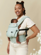 Parent is smiling whilst baby is fast asleep in the Tula Explore Carrier, being worn by the parent